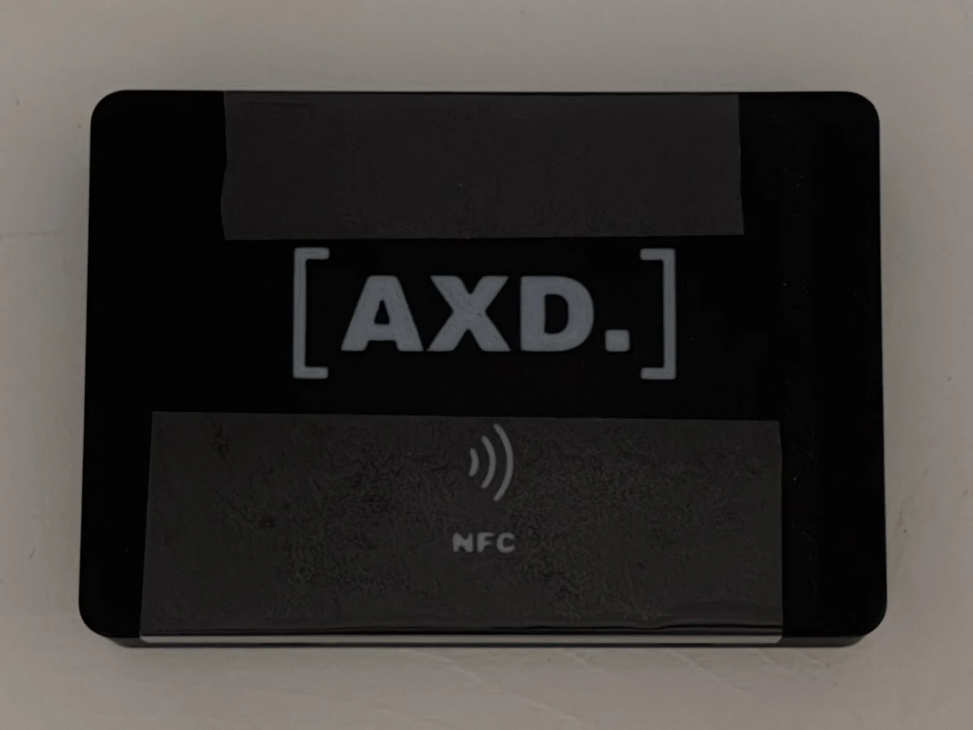 The rear of the real black PET enclosure, with white AXD lettering and the NFC symbol.